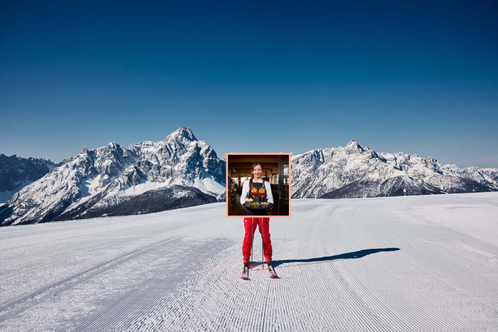 Photo: Arno Dejaco Snowy ski slope in front of the Sexten Dolomites, inset of a waitress carrying a tray.